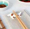 Chopsticks resting on a ceramic sausage dog–shaped chopstick rest.