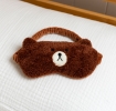 Brown plush teddy bear–shaped travel eye mask with embroidered facial features.