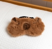 Light brown plush capybara‑shaped travel eye mask with stitched facial details