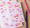 Pink notebook with colourful unicorns, rainbows, stars, and suns on the cover.