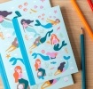Notebook with illustrated mermaids, sea creatures, and shells on a light aqua cover.