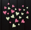 Pink and green glow‑in‑the‑dark heart shapes in assorted sizes on a black background.