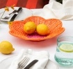 A shallow orange woven plastic basket with a flower-shaped rim and a pink centre.