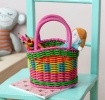 A small woven plastic basket with a pink handle and multicoloured striped body