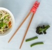 Training chopsticks with a bunny topper beside a bowl of noodles and vegetables.