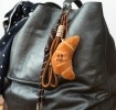 Plush croissant bag charm with brown cord strap and metal clip attachment