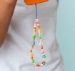 olourful beaded phone strap with smiley flower charms shown attached to an orange phone.