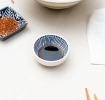 Round ceramic dipping bowl with blue line pattern shown with soy sauce.