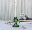 Green fish-shaped glass candlestick holding a lit white candle on a tabletop