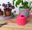Vibrant pink metal watering can with curved handle and long spout.
