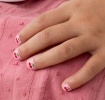 Red cherry printed nail stickers with pink background on a kid’s fingernails