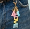 Gold keyring with colourful “LOVE” letter charm and pink and blue tassels.