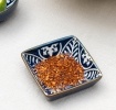 Square ceramic dipping bowl with a blue leaf pattern shown with chilli flakes.