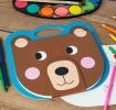 Brown bear-faced sketchbook with a blue handle, round ears, pink cheeks and smile.