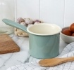Alt text: Pistachio green enamel milk pot with long handle on a kitchen worktop.