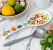 White ceramic spoon rest with a colourful fruit and leaf design.