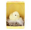 A fluffy yellow chick decoration sitting in a small wicker basket with an egg, displayed inside a yellow box.