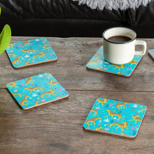 Four turquoise wood and cork coasters featuring cheetah pattern on table with drink