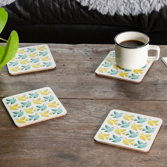 Four cream wood and cork coasters featuring bird pattern on table with drink