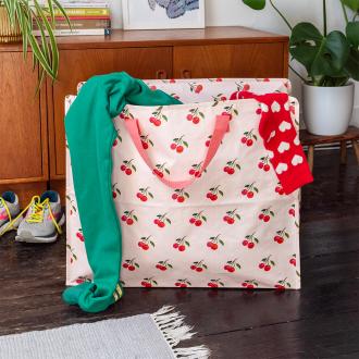 large rectangular bag with a cherry pattern on a light pink background filled with clothes