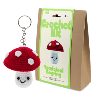 Crochet kit packaging displayed next to a finished red and white toadstool mushroom keychain