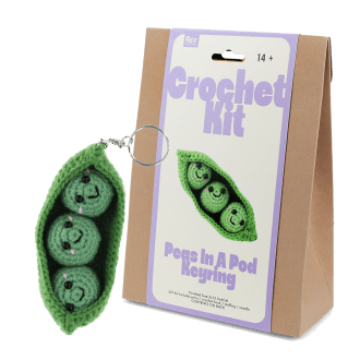 Crochet kit packaging placed beside finished green peas in a pod keychain 
