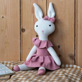 Knitted rabbit toy with long ears, wearing a pink dress with a ruffled collar and a matching bow on one ear