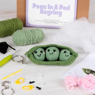 Crochet kit packaging placed beside finished green peas in a pod keychain 