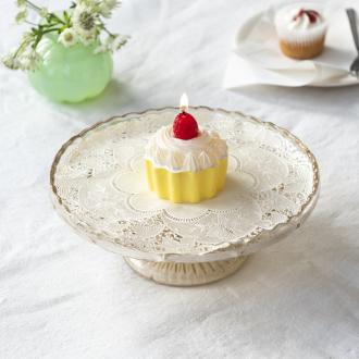 Cupcake‑shaped candle with white frosting and a strawberry topper displayed on a decorative cake stand