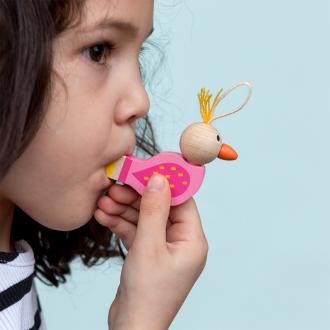 Child blowing a bird‑shaped wooden whistle with a pink body, wooden head, and orange beak.
