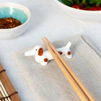 Chopsticks resting on a ceramic sausage dog–shaped chopstick rest.