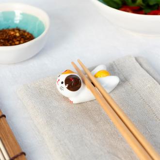 Chopsticks resting on a ceramic cat–shaped chopstick rest.