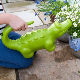 A large green crocodile watering can held outdoors.