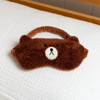 Brown plush teddy bear–shaped travel eye mask with embroidered facial features.