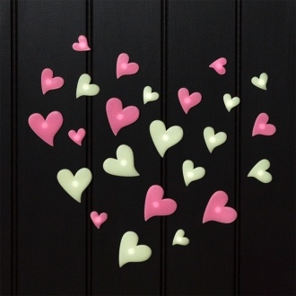 Pink and green glow‑in‑the‑dark heart shapes in assorted sizes on a black background.