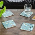Four blue-green wood and cork coasters featuring dog pattern on table with drink
