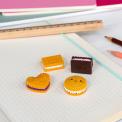 Four biscuit-shaped erasers in different styles and colours, placed on a notebook 