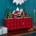 Red advent calendar with 24 gold-numbered drawers and a snowy village scene on top