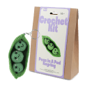 Crochet kit packaging placed beside finished green peas in a pod keychain 