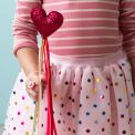 Kid holding a red heart wand with glittery top and ribbon streamers 