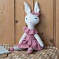 Knitted rabbit toy with long ears, wearing a pink dress with a ruffled collar and a matching bow on one ear