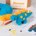 Completed blue crocheted dinosaur placed next to its packaging