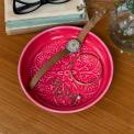 Vibrant pink enamel trinket dish displayed with a wristwatch and jewellery 