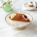 Brown pastry-shaped candle with cream and red cherry decorations displayed on a cake stand.
