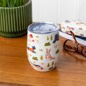 Travel cup with playful dog illustrations on a wooden table beside glasses and a matching case.