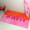 An orange and pink tufted bath mat with the word “BATH” in bold letters.