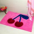 A pink tufted bath mat featuring a cherry motif.