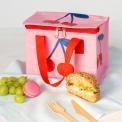A cherry‑themed insulated lunch bag placed on a table next to fruit.