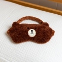 Brown plush teddy bear–shaped travel eye mask with embroidered facial features.