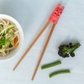 Training chopsticks with a bunny topper beside a bowl of noodles and vegetables.